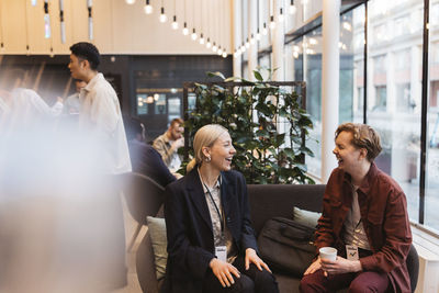 Happy male and female business delegates laughing while sitting on sofa at convention center