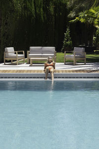 Vertical view of young woman laying in the edge of the swimming pool sun bathing to get tanned