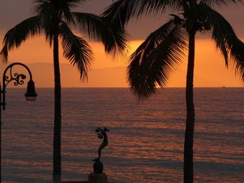 Silhouette palm trees against sea during sunset