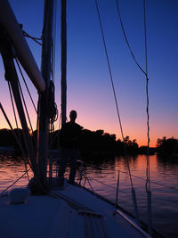 Silhouette man on sailboat against clear sky during sunset