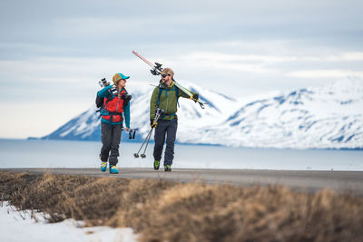 A couple walks down a road in iceland holding ski gear