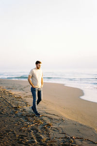 Rear view of man standing at beach against clear sky