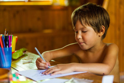 Shirtless boy drawing on paper