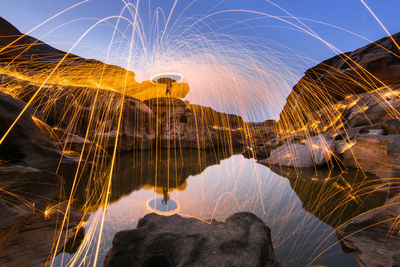 Light trails on rock against sky at night