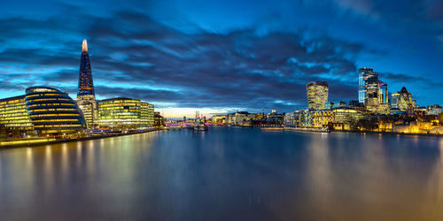 Illuminated buildings in city against cloudy sky