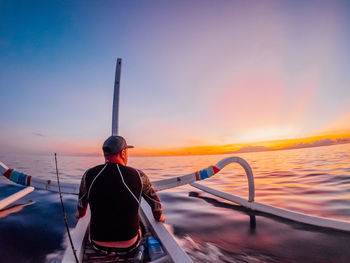 Rear view of man on sea against sky during sunset