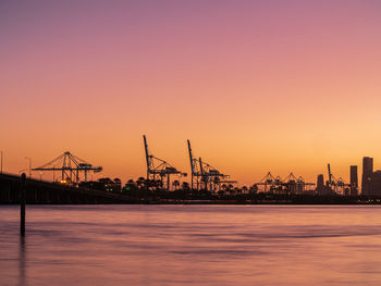 Cranes at commercial dock against sky during sunset