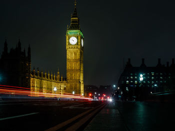 Light trails over road by illuminated big ben against sky at night in city