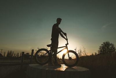 Silhouette man riding bicycle against sky during sunset