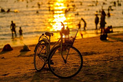 Silhouette bicycle on beach against sky during sunset
