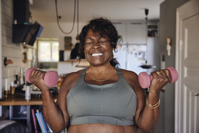 Mature woman clenching teeth while exercising with dumbbells at home