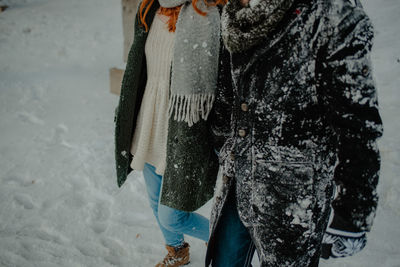 Midsection of couple holding hands walking on snow covered land in forest