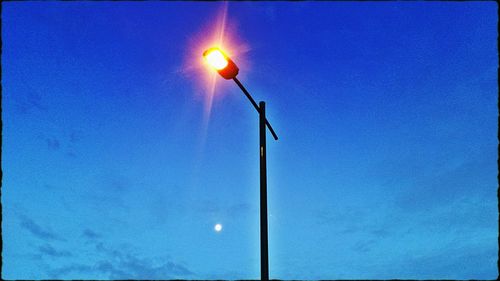 Low angle view of illuminated street light against blue sky