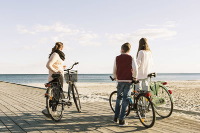 Full length of friends with bicycles on boardwalk at beach