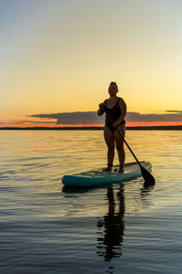 Man rowing on sea against sky during sunset