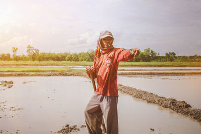 Farmer pointing while standing on field against sky