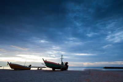 Boat moored on beach against sky during sunset