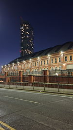 Illuminated building by street against sky at night