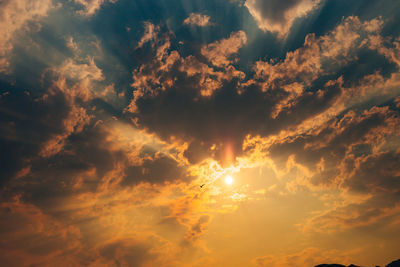 Low angle view of sunlight streaming through clouds during sunset