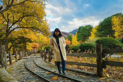 Portrait of woman standing by railroad tracks against sky