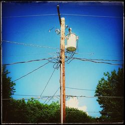 Low angle view of electricity pylon against blue sky