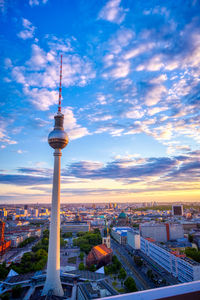 Communications tower in city against sky during sunset