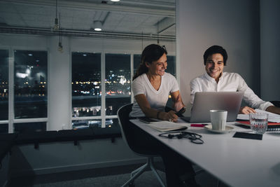 Smiling businessman and businesswoman planning strategy while looking at laptop in office