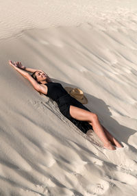 Young female tourist lying down on sandy hill while exploring dunes of corralejo at sundown in fuerteventura canary islands spain