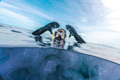 A woman in a black wetsuit is in the water with jellyfish. the jellyfish are floating around her