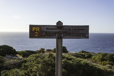 Information sign on wooden post by sea against sky