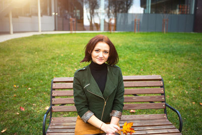 Portrait of young woman sitting on bench in park