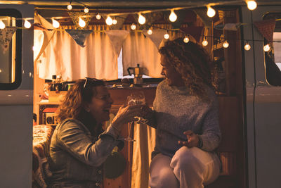 Male and female friends toasting while sitting by motor home at night