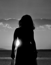 Rear view of silhouette woman standing at beach against sky
