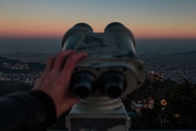 Midsection of man holding cityscape against sky during sunset