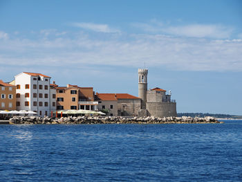 Sea by buildings in city against sky