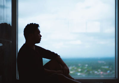 Side view of thoughtful man sitting on window sill