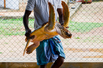 Man holding fish while standing by chainlink fence