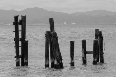 Wooden posts in sea against mountains