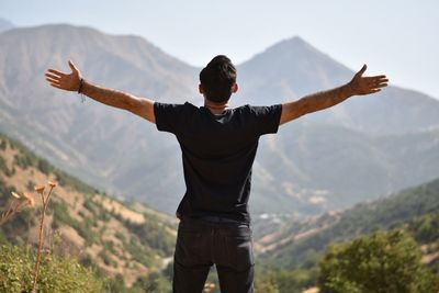 Rear view of man with arms outstretched against mountains