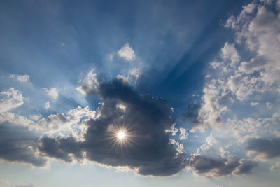 Low angle view of sunlight streaming through clouds