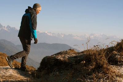 Man standing on rock looking at mountains against sky