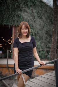 Portrait of young woman standing against railing