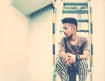 Young man looking away while standing against wall