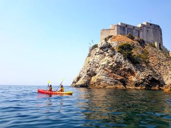 Men on rock in sea against clear sky