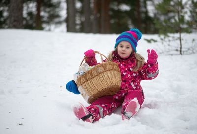 Portrait of smiling girl holding basket while sitting on snow