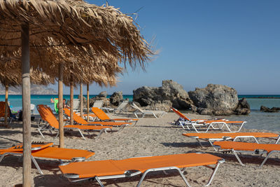 Lounge chairs on beach against clear sky