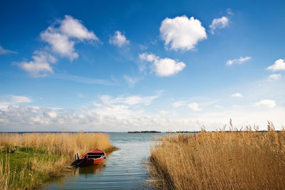 Boat moored at calm lake against blue sky