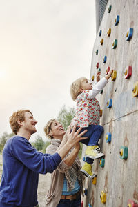 Girl climbing on a wall supported by parents