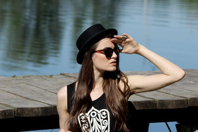 Young woman in sunglasses looking away while standing by lake