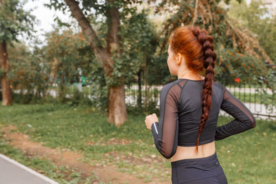 Young attractive girl in sports tight clothes doing exercises in the park among green foliage